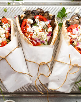 Three gyros on tray wrapped in paper with twine.