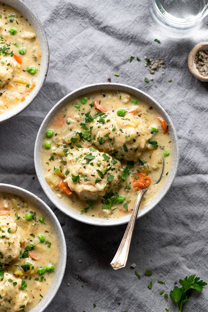3 bowls of creamy vegetable soup with dumplings with spoon and parsley garnish.