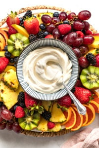 Bowl of mascarpone fruit dip on board surrounded by fruit.
