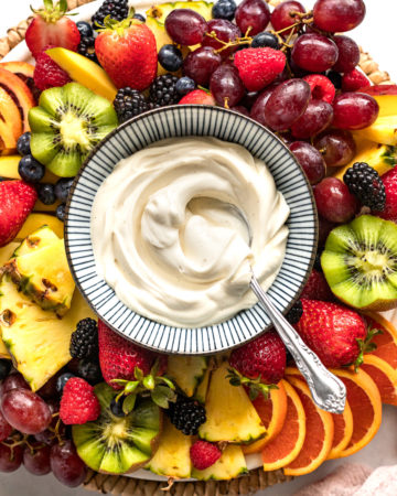 Bowl of mascarpone fruit dip on board surrounded by fruit.