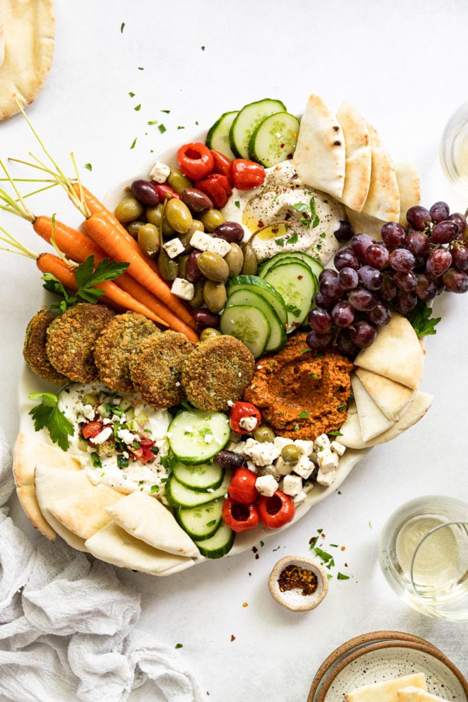 Vegetarian mezze platter next to wine glasses and pita bread.