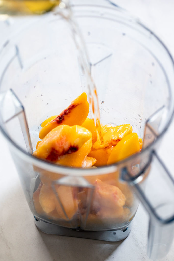 Wine pouring into blender of peaches.