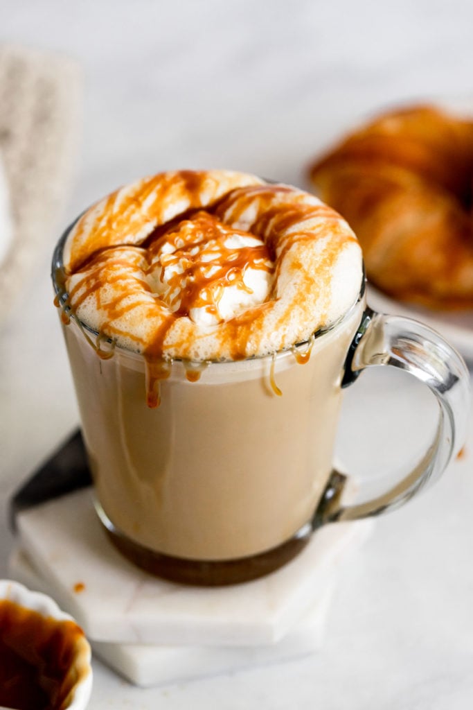 Caramel latte next to croissant with whipped cream and caramel drizzle.