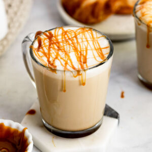 Mug of caramel latte with drizzle and plate of croissants.