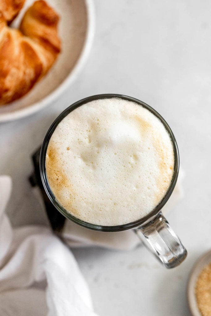 Overhead latte with foam next to croissant.