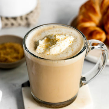 Vanilla latte with whipped cream next to sugar and croissants
