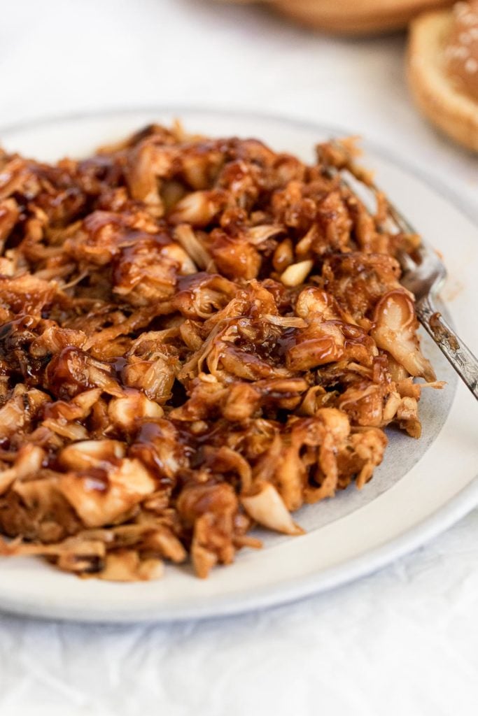 Plate of shredded jackfruit tossed in bbq sauce with fork.