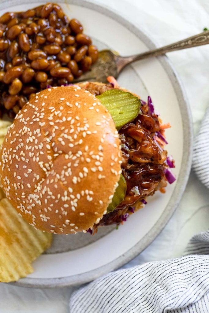 BBQ sandwich on plate with baked beans and chips.