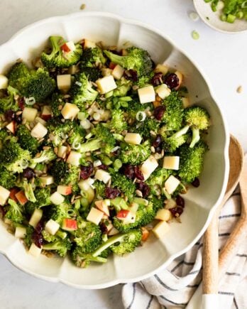 Broccoli salad in large bowl next to serving spoons and linen.
