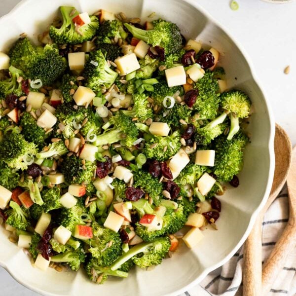 Broccoli salad in large bowl next to serving spoons and linen.