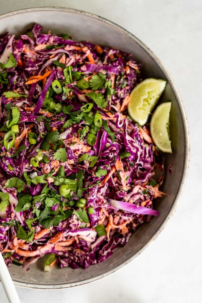 Up close bowl of coleslaw with lime wedges.