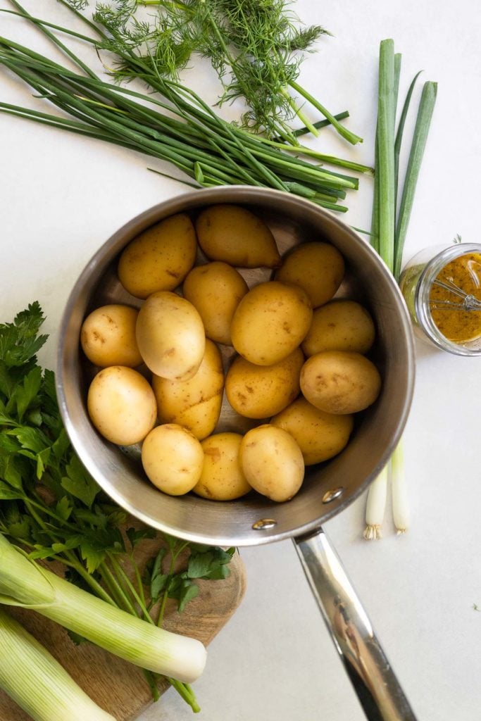 Saucepan with baby yukon gold potatoes next to herbs and leek.