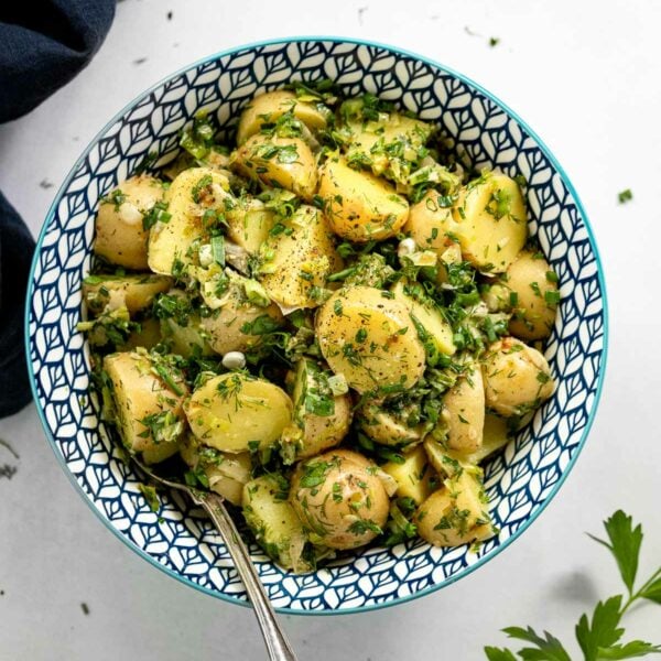 Bowl of potato salad next to parsley and blue linen.