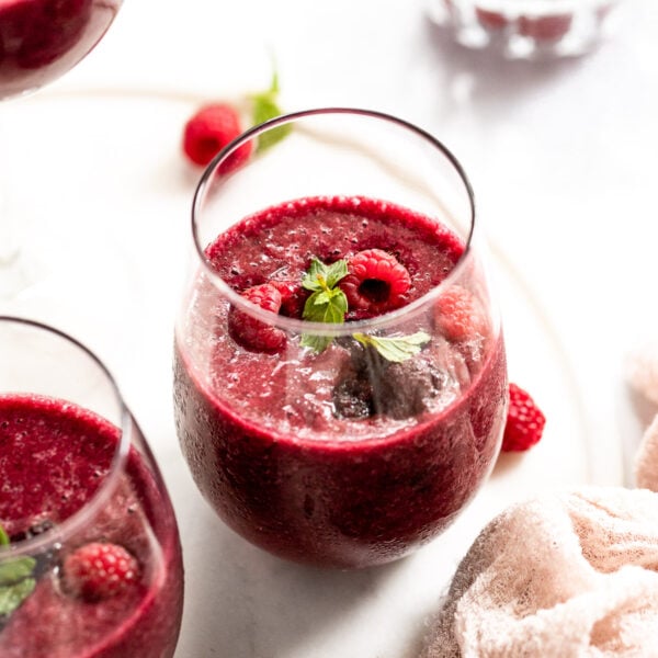 Three red wine slushies next to bowl of raspberries.