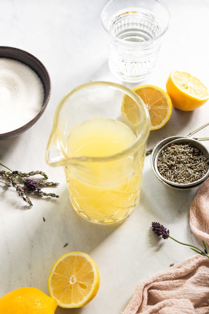 Fresh lemon juice in pitcher next to sugar and lavender.