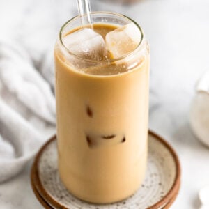 Iced latte with straw on plate next to spoon and linen.