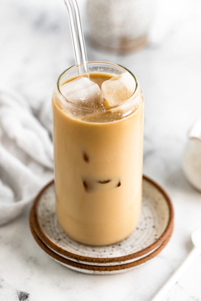 Iced latte with straw on plate next to spoon and linen.