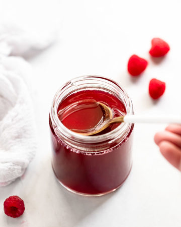 Raspberry syrup with spoon lifting up.