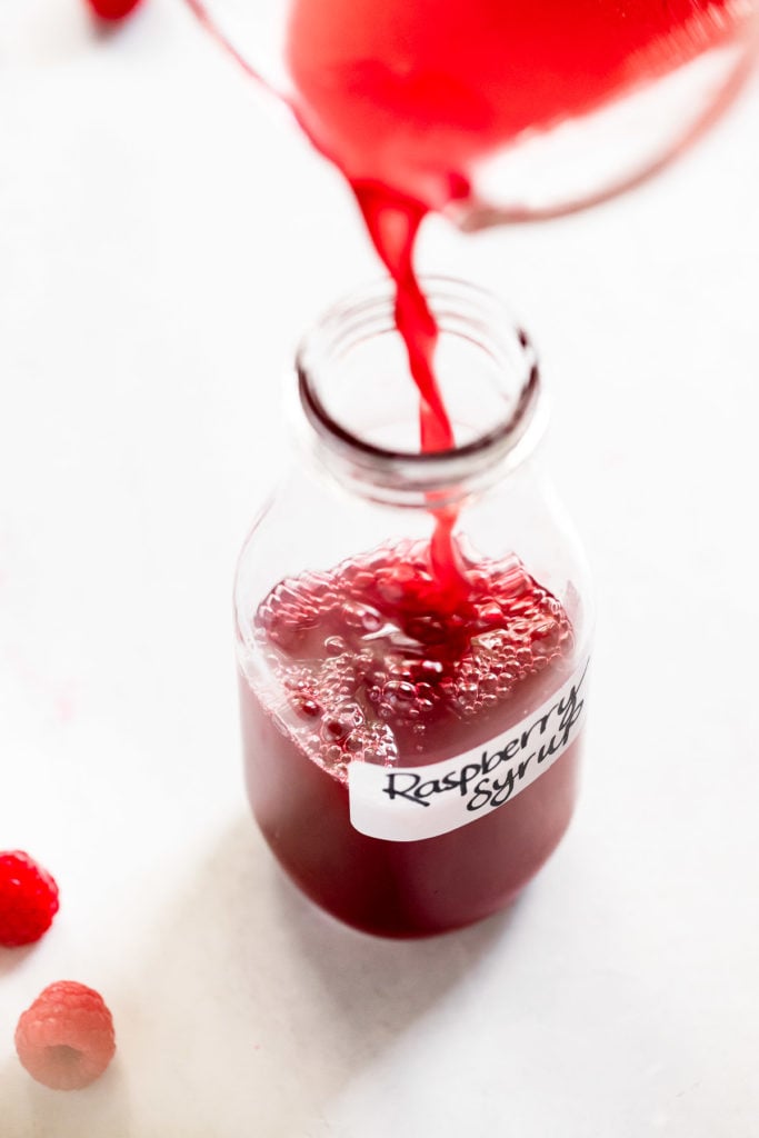 Raspberry syrup pouring into jar with label.