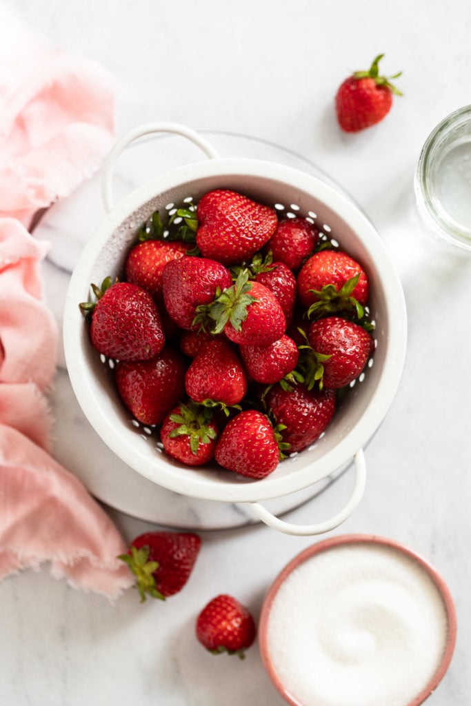 Bowl of strawberries next to sugar and water.