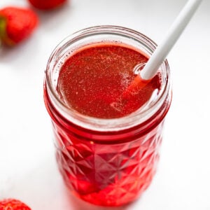 Jar of strawberry simple syrup with spoon.