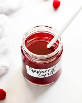 Jar of raspberry syrup with label on it and spoon inside.