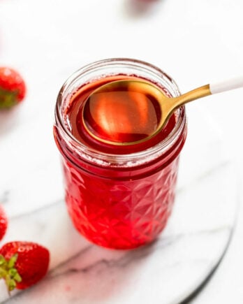 Jar of strawberry syrup with spoon dipping out.