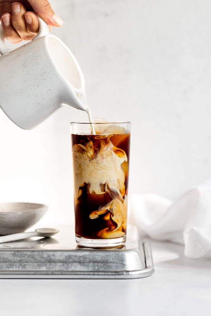 Cream pouring into glass of cold coffee.