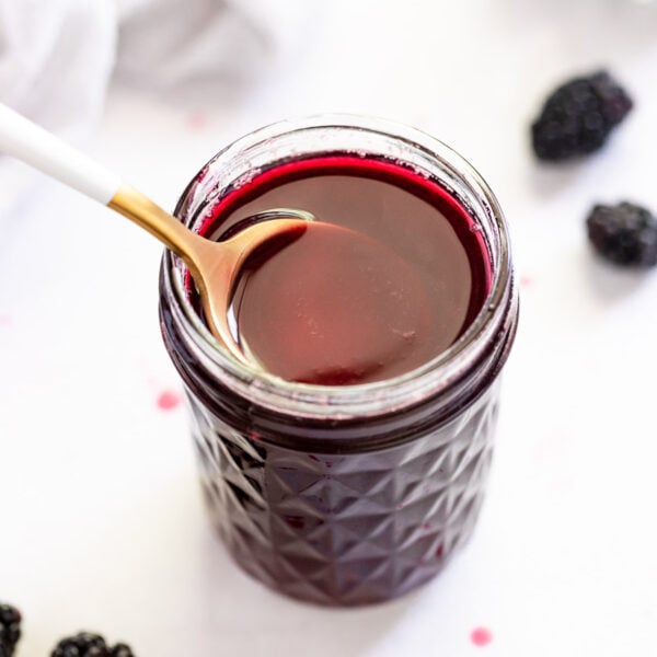 Spoon going into jar of blackberry syrup.