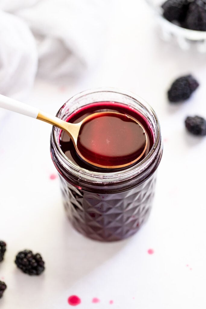 Blackberry syrup in jar with spoon scooping.