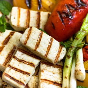 Grilled halloumi cheese slices on plate with grilled vegetables.