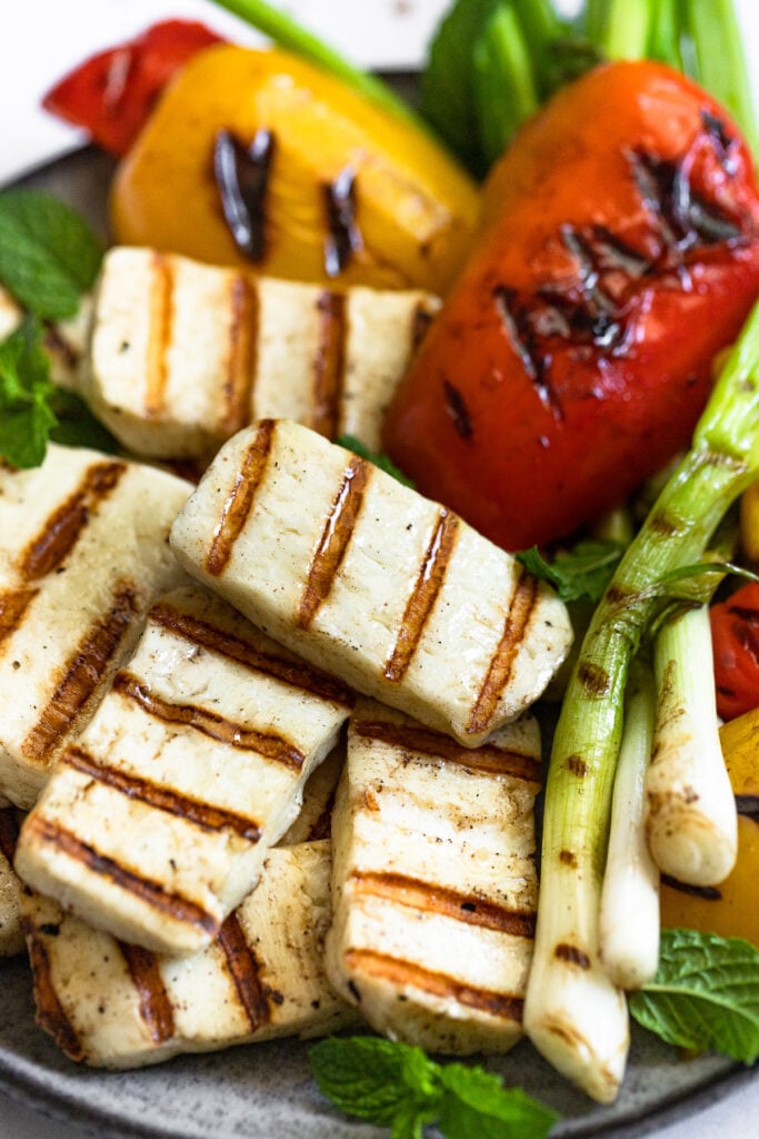 Grilled halloumi cheese slices on plate with grilled vegetables.