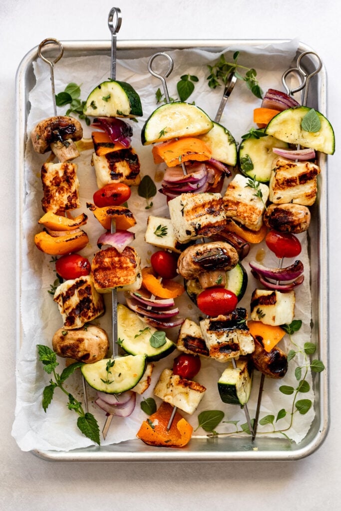 Baking pan with kebabs laid across with fresh herbs.