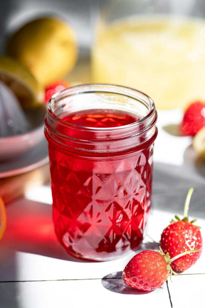 Strawberry syrup in jar next to berries.