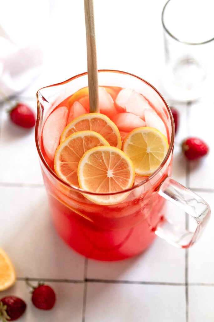 Pitcher of strawberry lemonade with lemon slices and spoon.