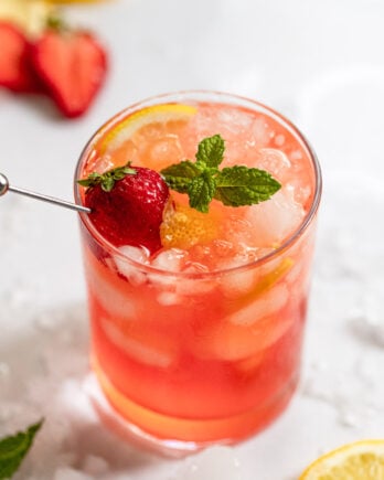 Glass of strawberry vodka lemonade with mint, strawberry, and lemon garnish.