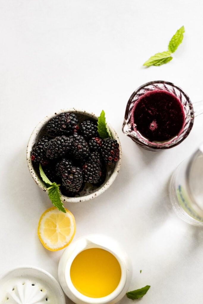 Bowl of blackberries next to blackberry syrup and lemon juice.