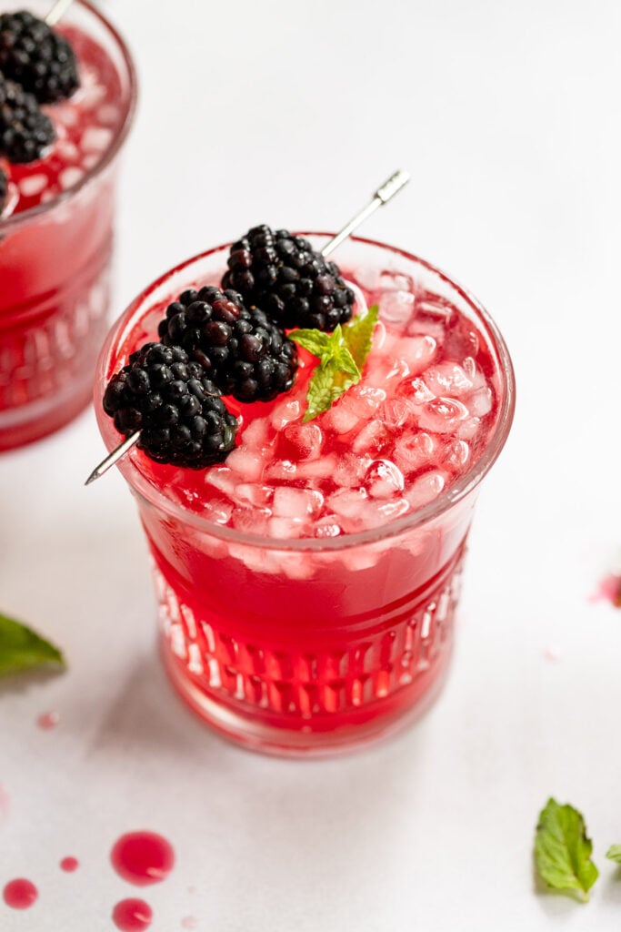 Two cocktails with mint and berry garnish.