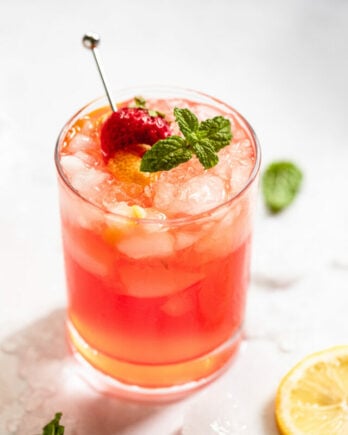 Glass of strawberry vodka lemonade with mint, strawberry, and lemon garnish.