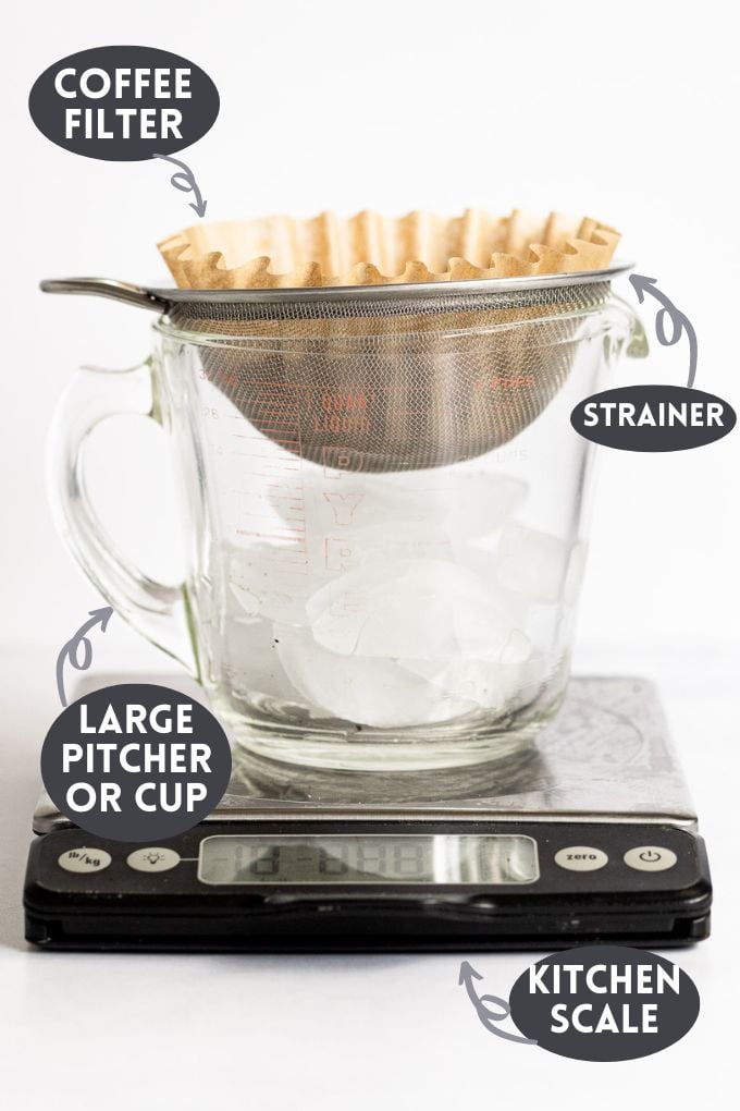 Kitchen scale with large measuring cup on top filled with ice topped with strainer and filter.