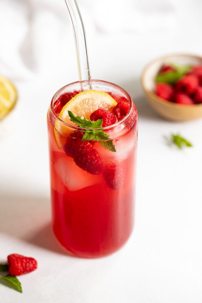 Raspberry Iced Tea in glass with berries, lemon, and mint.