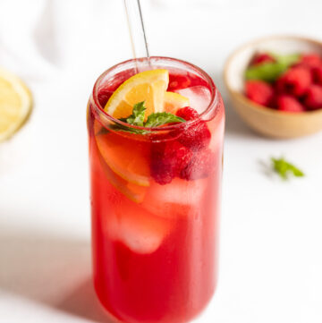 Raspberry Iced Tea in glass with berries, lemon, and mint.