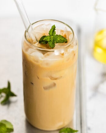 Iced mint latte in glass with straw and mint leaf.