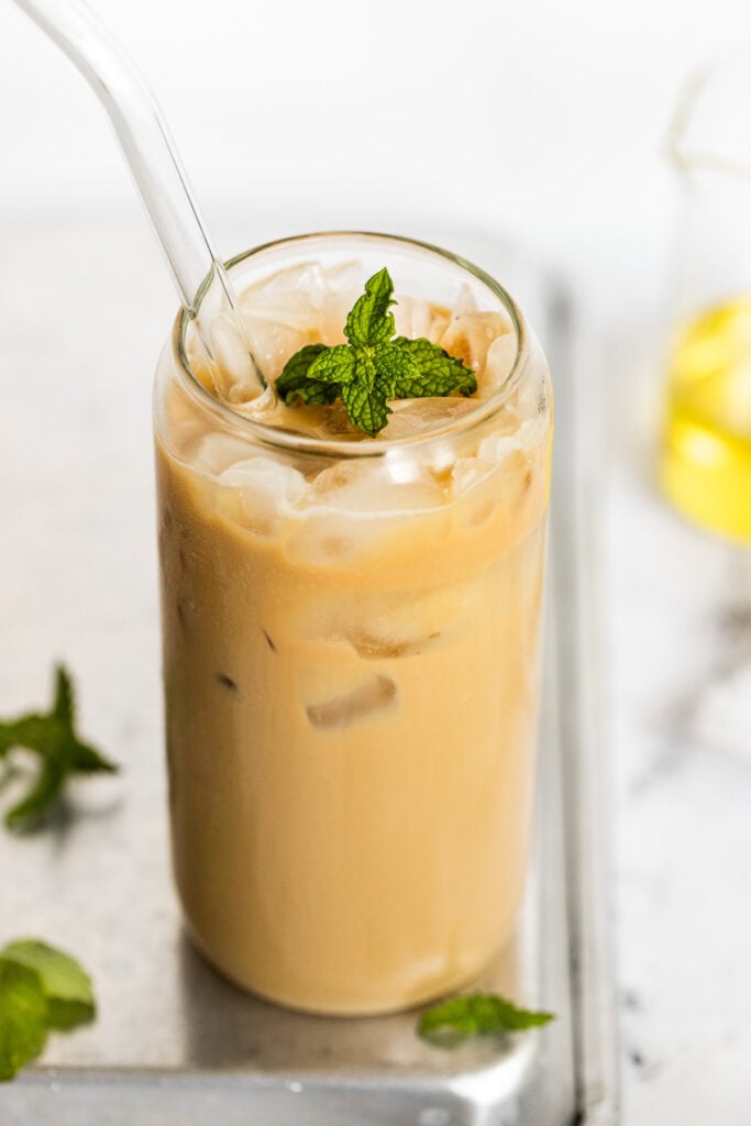 Iced mint latte in glass with straw and mint leaf.