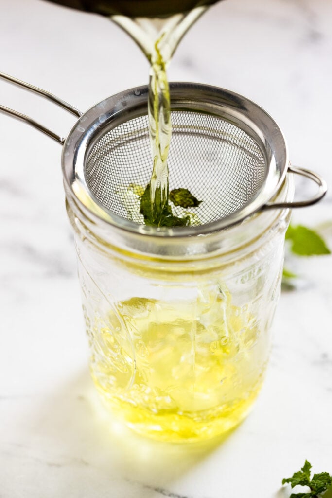 Mint syrup pouring into jar through strainer.
