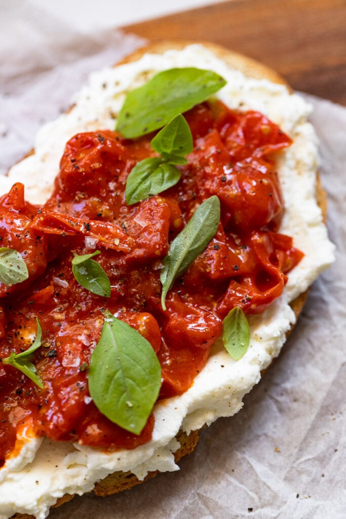 Blistered tomato sauce on ricotta toast with fresh basil leaves.