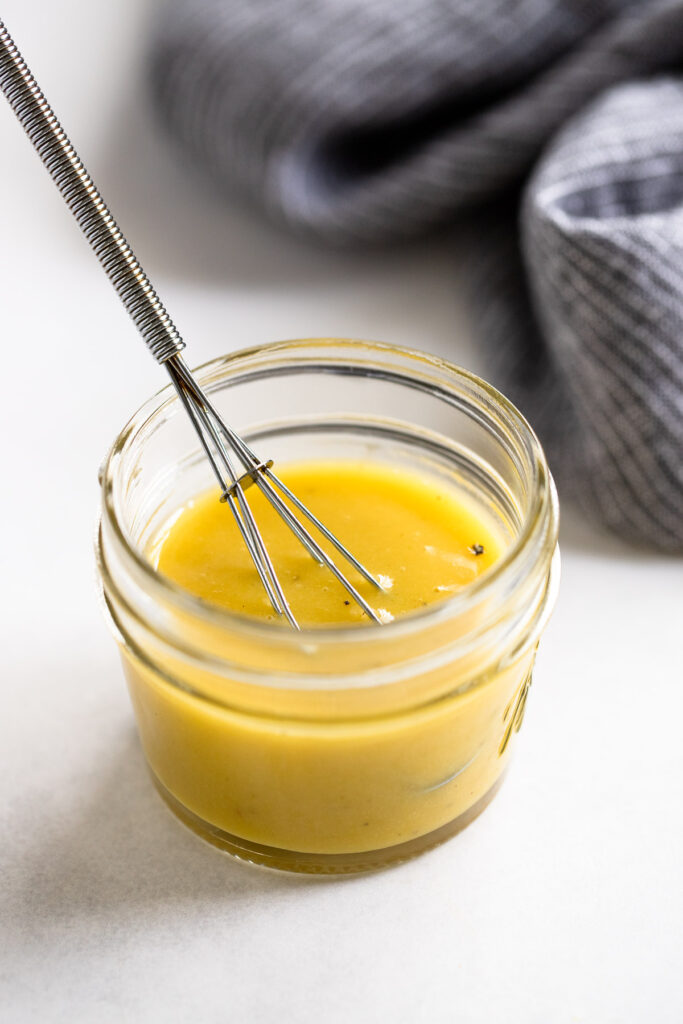 Jar of honey mustard dressing with whisk.