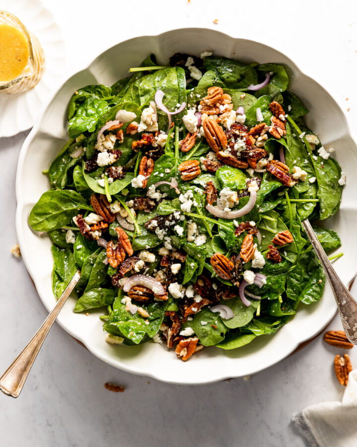 Bowl of spinach salad with serving spoons.