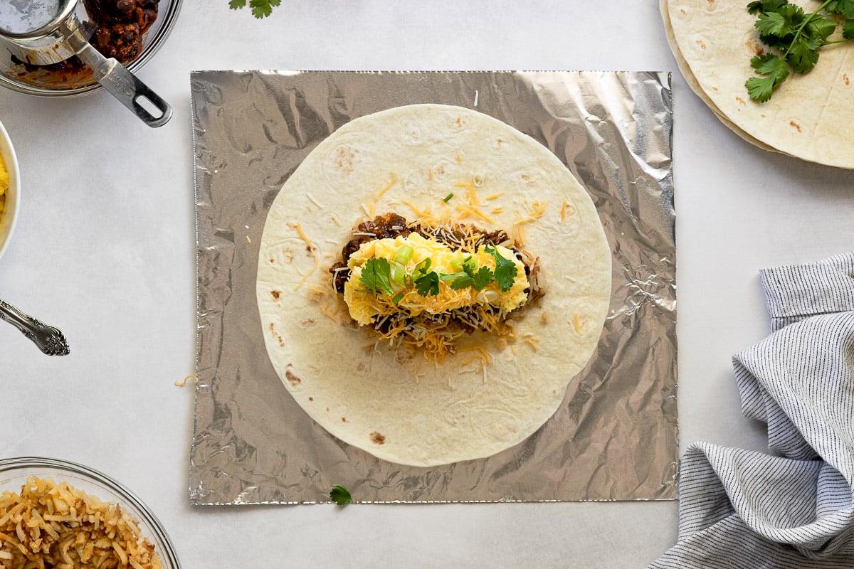 Tortilla with burrito fillings on piece of foil.