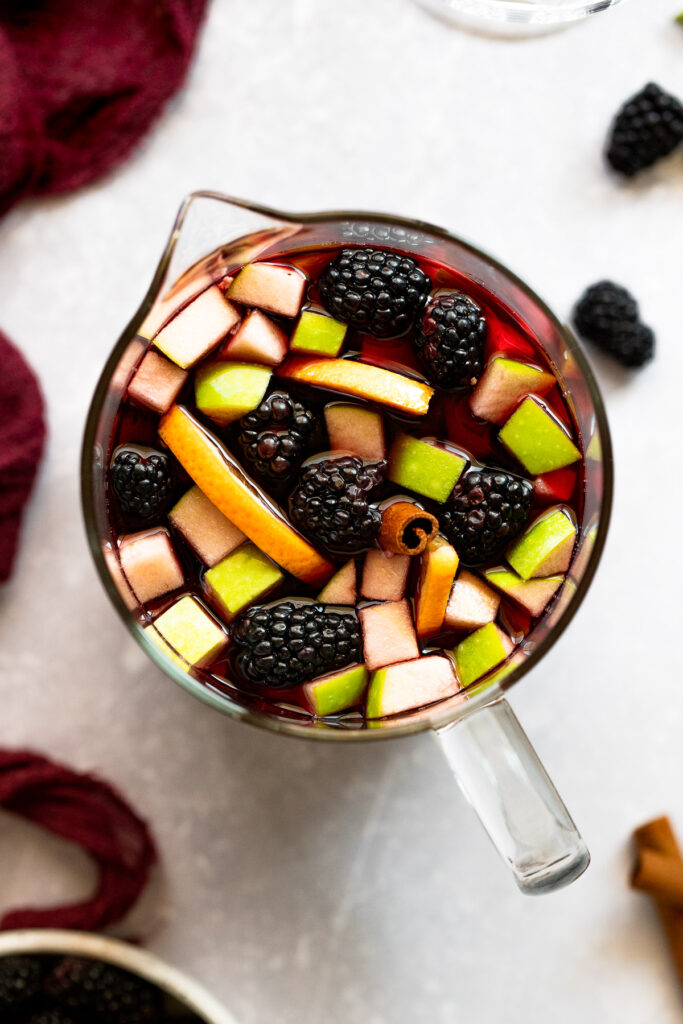 Pitcher of blackberry sangria with apples, cinnamon stick, oranges, and blackberries.